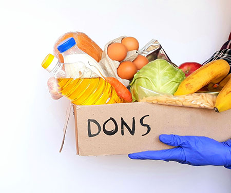 Main gantée offrant une boîte de denrées alimentaires en dons